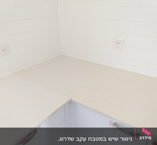 משטח שיש בהיר מותקן בפינת מטבח על ארונות לבנים